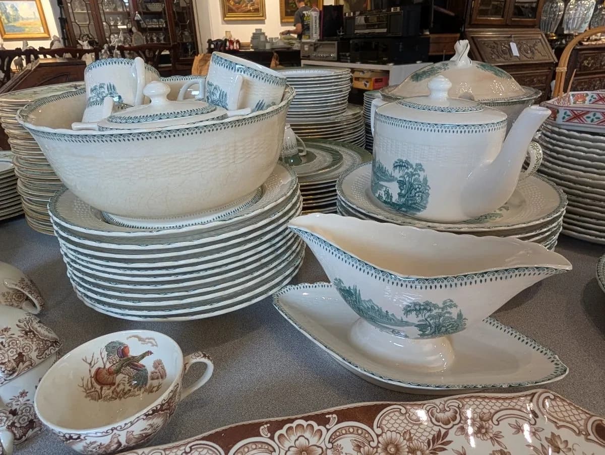 Green transferware china — tureens, teapot, and gravy boat — laid out at a Houston estate sale