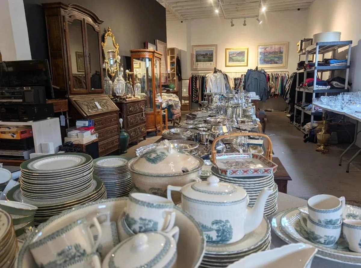 Estate sale floor in Houston — stacked china, silver holloware, framed art, and racks of clothing