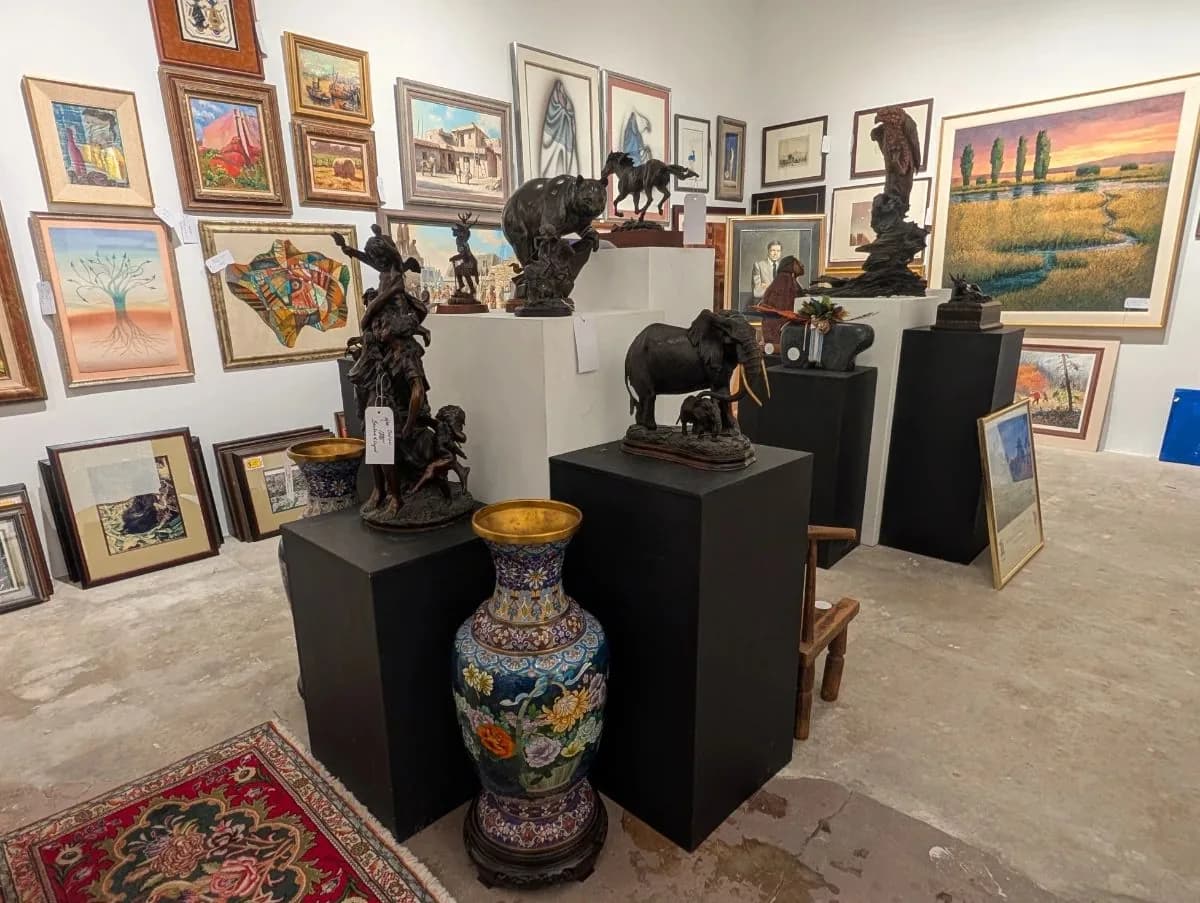 Bronze sculptures on pedestals beneath a wall of framed paintings at a Reeves Estates sale